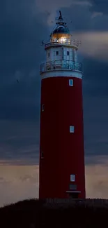 Lighthouse stands illuminated beneath stormy navy blue sky.