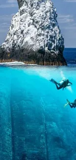 Two divers explore rocky underwater scene with towering ocean rock.