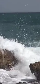 Ocean wave crashing on rocky shore with splashes and blue sea.