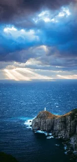 Lighthouse perched on rocky cliffs with dramatic sky and sun rays over the ocean.