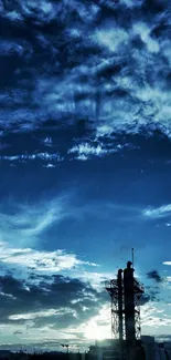 Tall silhouetted tower against a deep blue sky with dramatic clouds at dusk.