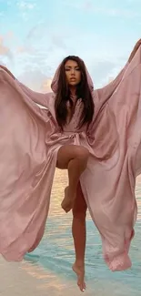 Woman in flowing pink robe on a beach.