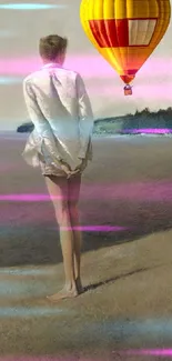 Figure standing on beach with vibrant hot air balloon overhead.