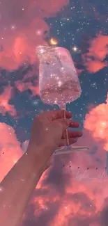 Hand holding a sparkly glass beneath a dreamy pink sky.