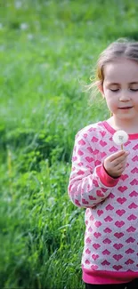 Child holding a dandelion in a vibrant green field.