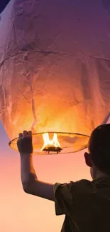 A child holds a glowing paper lantern against a vibrant sunset sky.