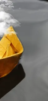 Yellow paper boat floating on calm gray water with clouds overhead.