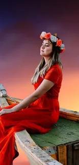 Woman in red dress with floral crown on boat at sunset.