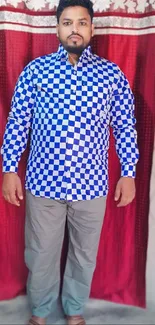 Man in blue checkerboard shirt against red curtain.