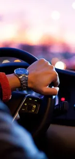 Hand steering at sunset with blurred city lights.