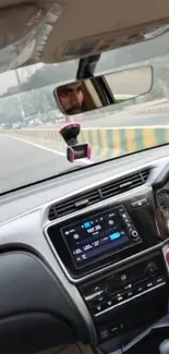 Car interior view with dashboard and rear view mirror on road.