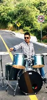 Drummer playing on scenic road surrounded by nature.