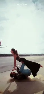 Couple performing acrobatics on an airport runway with a plane in the background.