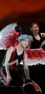 Performer with red angel wings on stage during a dynamic show.