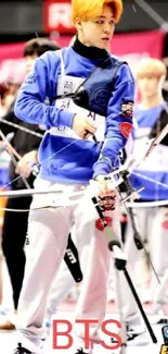 Athlete in blue tracksuit aiming archery bow at event.