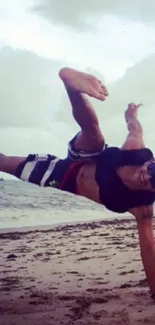 Man performing a handstand on a beach with ocean waves in the background.