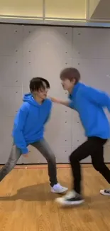 Dynamic dance duo in blue hoodies on wooden floor.