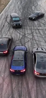 Five cars performing drift maneuvers on a racetrack, creating tire marks.