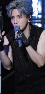 Concert performer with mic on stage with black attire and gloves.