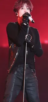 Performer in black outfit singing on a red-lit stage.