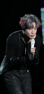 Performer passionately singing on stage in a dramatic black outfit.