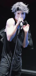 Performer with a microphone on stage in a dramatic black attire.