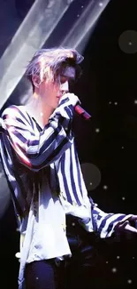 Performer with striped outfit holding a microphone under dramatic stage lights.