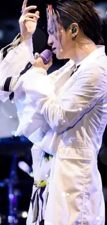 Singer in white coat performing live on stage with a microphone.