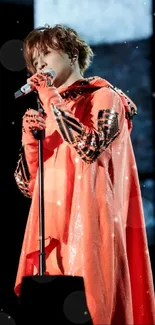 Performer in red cloak singing on stage with microphone.