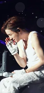 Performer in white attire on stage with dramatic lighting.