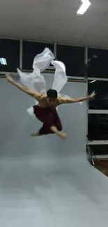 Dancer performing a high leap in a studio with a white backdrop.