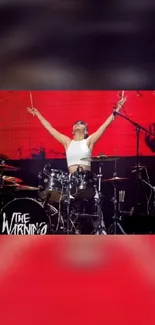 Drummer performing energetically on stage with a red backdrop.