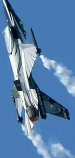 Fighter jet performing aerial maneuvers in clear blue sky with cloud trails.