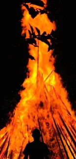 Silhouette in front of blazing orange fire at night.