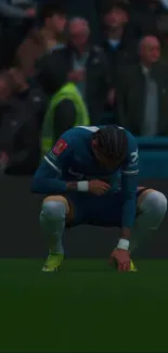 Crouching football player on green field during a match, deep blue tones.