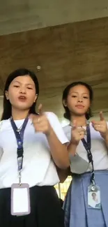 Two young women in white shirts making playful hand gestures indoors.