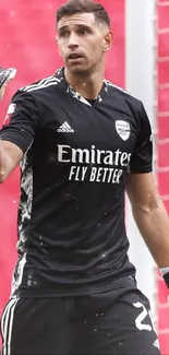 Goalkeeper in black uniform with red stadium background.