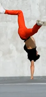 Person performing a handstand in red pants on concrete.