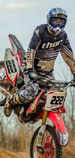 Motocross rider performing a stunt on a dirt trail with a red and white bike.