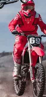 Red motocross rider jumping on a dirt bike in action against a scenic backdrop.