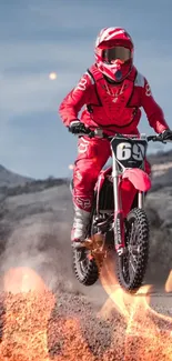 Motocross rider in red gear soaring over a flaming dirt track.