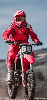 Motocross racer in red gear riding on a dirt trail with scenic background.