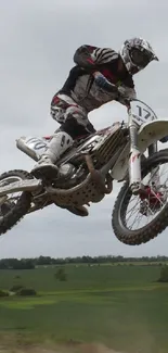 Motocross rider jumps high in the air on a dirt bike against a green landscape.