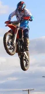 Motocross rider jumps high against a blue sky in dynamic wallpaper.