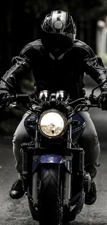 Motorcycle rider in black leather gear on a dark road.