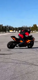 Motorcyclist performs a thrilling stunt on an orange bike in an open area.