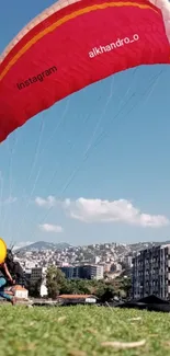 Vibrant red paraglider over cityscape under blue sky.