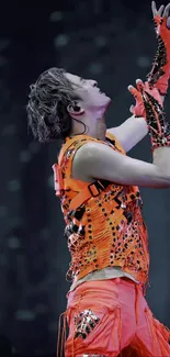 Performer in vibrant orange attire striking a dynamic pose on stage.