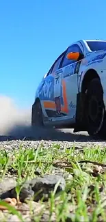 Rally car speeding on gravel with blue sky backdrop and green grass.