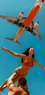 Couple posing under a flying airplane in blue sky.